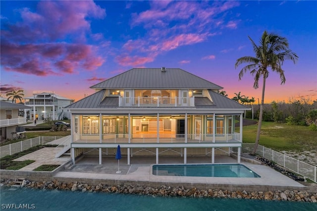 back house at dusk with a patio, a balcony, and a pool with hot tub