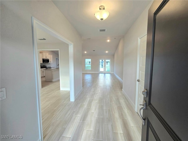 hall with visible vents, light wood-style floors, and baseboards