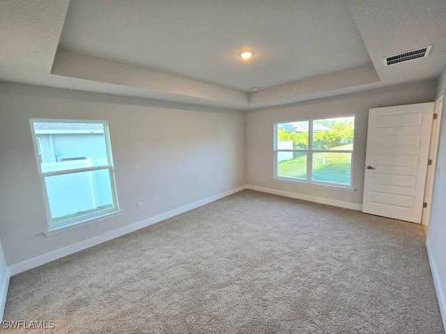 unfurnished room with a tray ceiling, baseboards, and visible vents