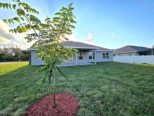 back of house featuring stucco siding, a lawn, and fence