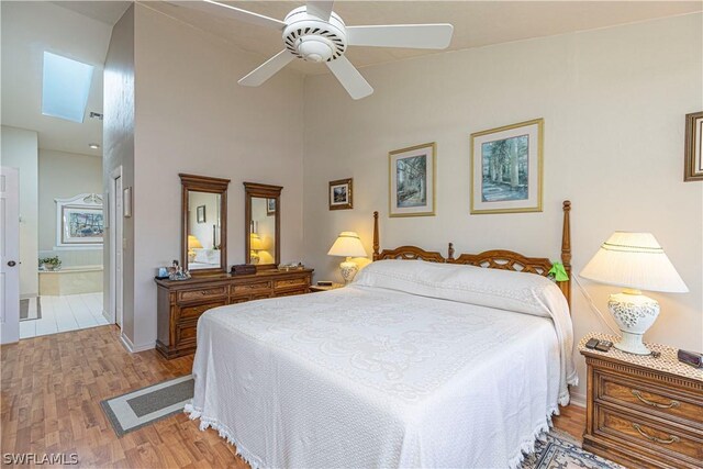 bedroom with light hardwood / wood-style flooring, a high ceiling, connected bathroom, a skylight, and ceiling fan