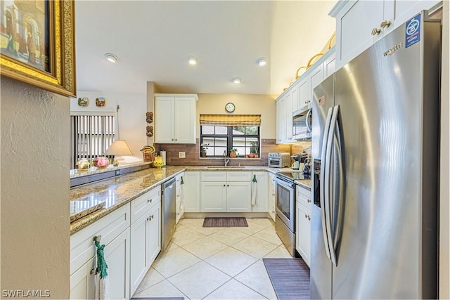 kitchen with white cabinets, appliances with stainless steel finishes, light stone countertops, and decorative backsplash