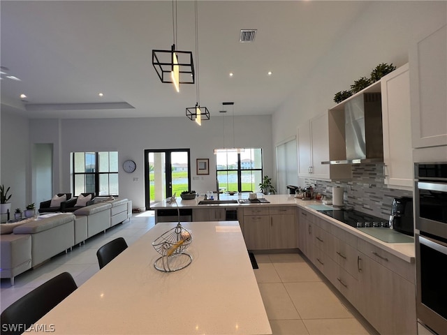 kitchen with wall chimney range hood, tasteful backsplash, pendant lighting, and light tile floors