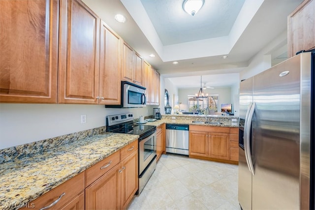 kitchen featuring light tile flooring, stainless steel appliances, a tray ceiling, light stone countertops, and sink