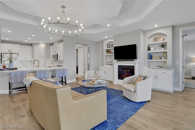 living room with a tray ceiling, a notable chandelier, light hardwood / wood-style flooring, and built in shelves