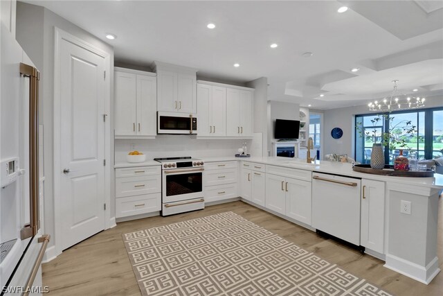 kitchen featuring kitchen peninsula, white cabinetry, a chandelier, light hardwood / wood-style floors, and white appliances