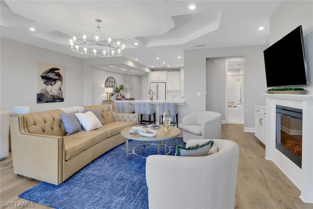 living room featuring an inviting chandelier, a tray ceiling, and light wood-type flooring