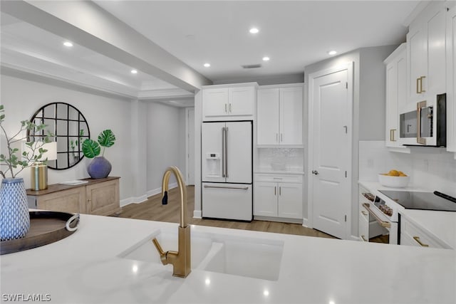 kitchen featuring decorative backsplash, white cabinetry, light hardwood / wood-style flooring, and white appliances