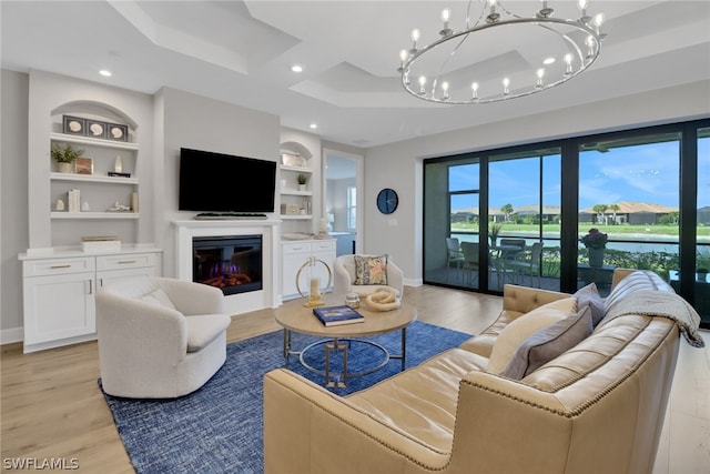 living room with light hardwood / wood-style flooring, a notable chandelier, a tray ceiling, and built in shelves