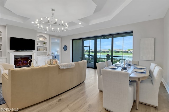 living room with a tray ceiling, a notable chandelier, built in features, and light hardwood / wood-style flooring