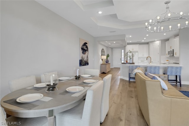 dining space with a tray ceiling, light hardwood / wood-style flooring, and a chandelier