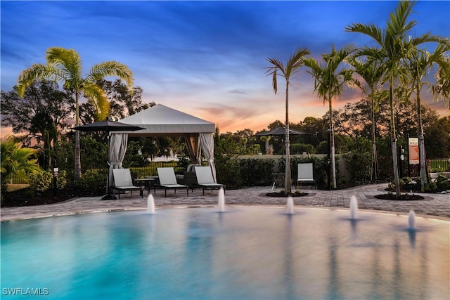 pool at dusk featuring a gazebo, pool water feature, and a patio