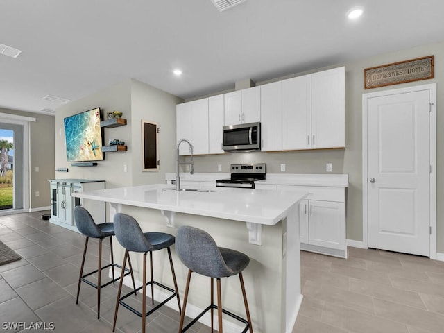 kitchen featuring white cabinets, a center island with sink, appliances with stainless steel finishes, and light tile flooring