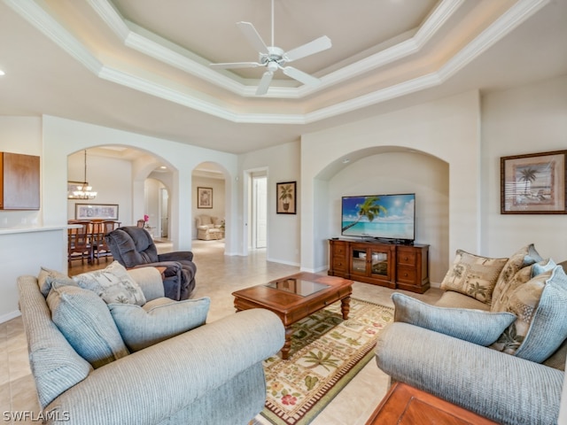 living room featuring ornamental molding, ceiling fan with notable chandelier, and a tray ceiling