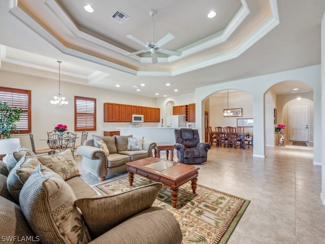 tiled living room featuring ceiling fan with notable chandelier, ornamental molding, a wealth of natural light, and a tray ceiling