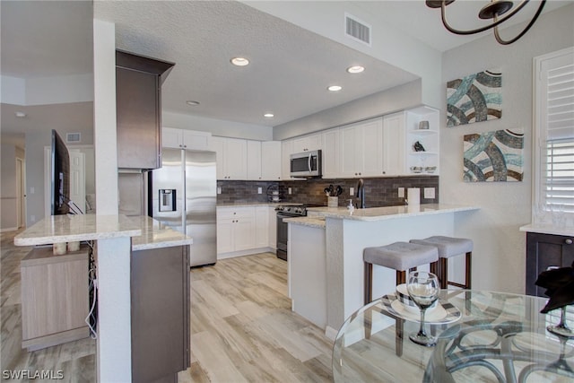 kitchen featuring light stone counters, stainless steel appliances, visible vents, light wood-type flooring, and a peninsula