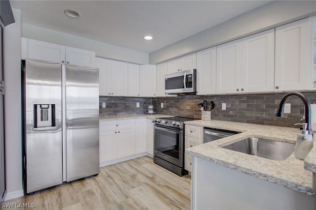 kitchen with appliances with stainless steel finishes, white cabinetry, a sink, and light stone countertops