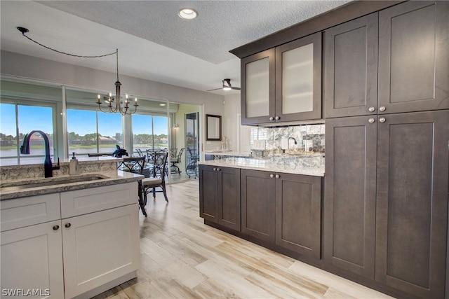 kitchen featuring light wood finished floors, hanging light fixtures, an inviting chandelier, a sink, and light stone countertops