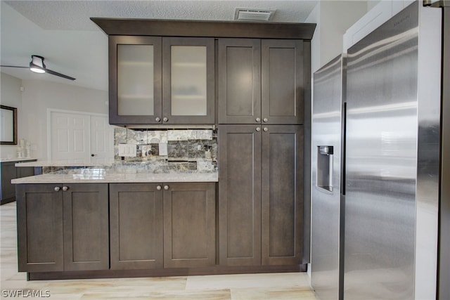 kitchen with visible vents, dark brown cabinets, backsplash, stainless steel fridge, and glass insert cabinets