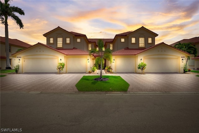 mediterranean / spanish home with a garage, a tile roof, and decorative driveway