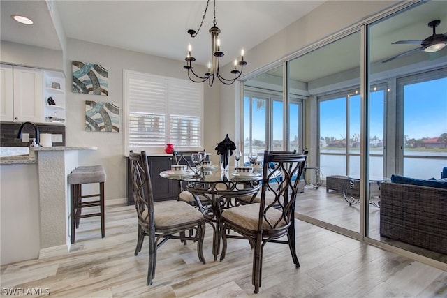 dining room featuring light wood-type flooring, a water view, baseboards, and ceiling fan with notable chandelier