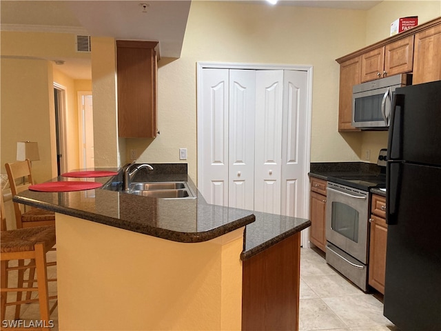 kitchen featuring brown cabinets, a breakfast bar area, appliances with stainless steel finishes, a sink, and a peninsula