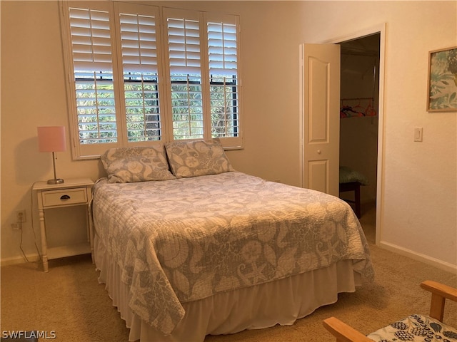 bedroom with light colored carpet, a spacious closet, baseboards, and multiple windows