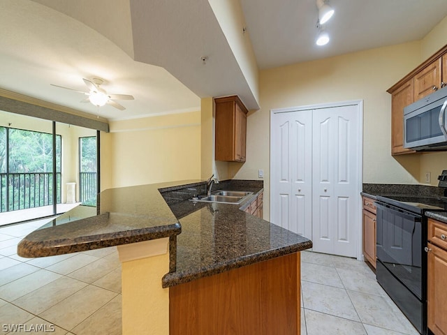 kitchen with brown cabinets, black electric range oven, stainless steel microwave, a sink, and a peninsula