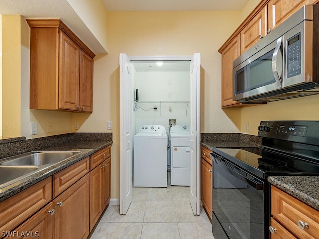 kitchen featuring stainless steel microwave, brown cabinets, dark stone countertops, washing machine and clothes dryer, and black / electric stove