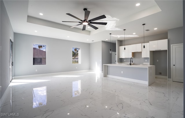 kitchen with white cabinets, a kitchen island with sink, and a raised ceiling