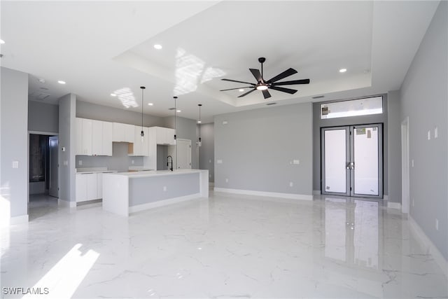 unfurnished living room with french doors, sink, ceiling fan, and a tray ceiling