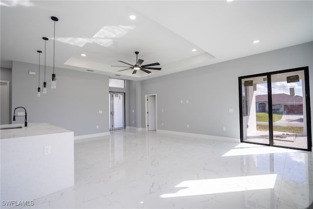 unfurnished living room with sink, a raised ceiling, and ceiling fan