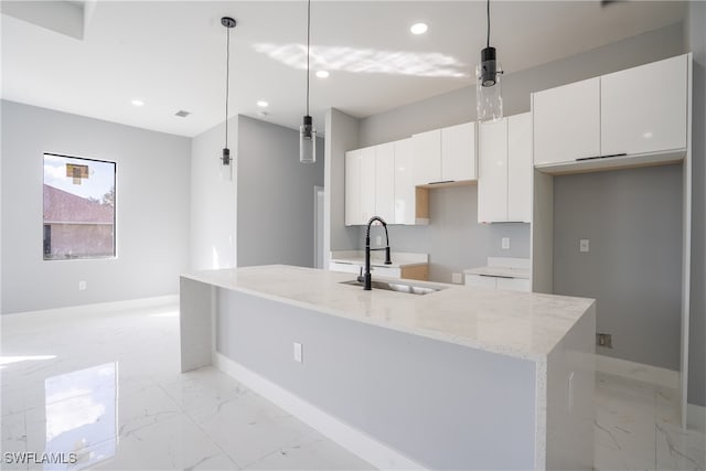 kitchen featuring white cabinetry, hanging light fixtures, sink, and an island with sink