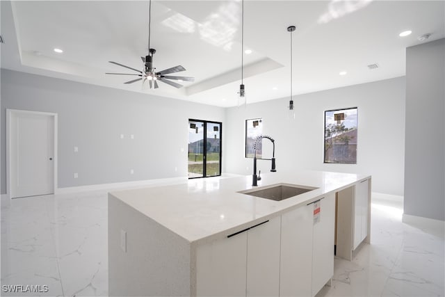 kitchen with white cabinetry, a raised ceiling, pendant lighting, sink, and an island with sink