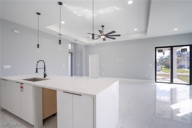 kitchen with a tray ceiling, white cabinetry, pendant lighting, and sink