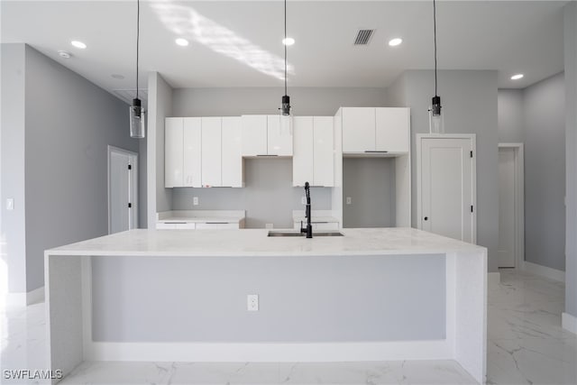 kitchen featuring a kitchen island with sink, sink, decorative light fixtures, and white cabinets