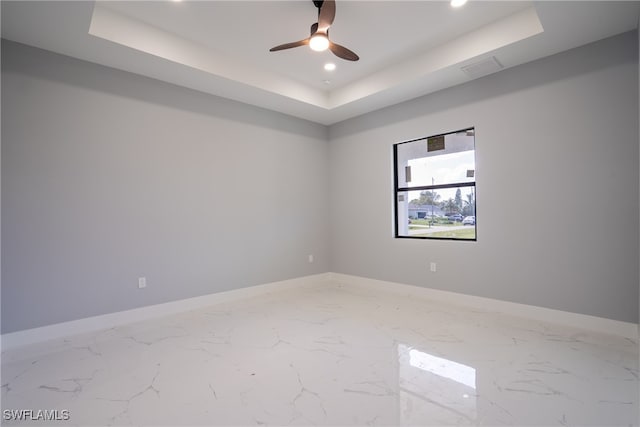 unfurnished room with ceiling fan and a tray ceiling