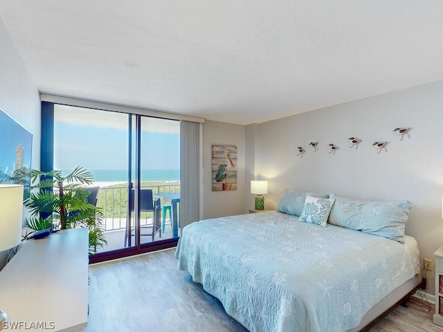 bedroom with hardwood / wood-style flooring, a water view, and access to exterior