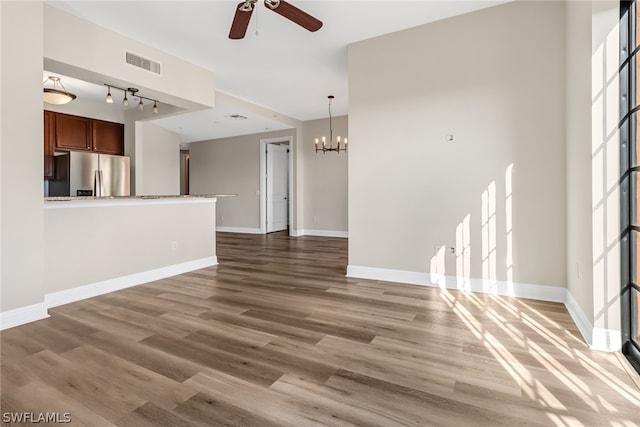 unfurnished living room with ceiling fan with notable chandelier, wood-type flooring, and track lighting