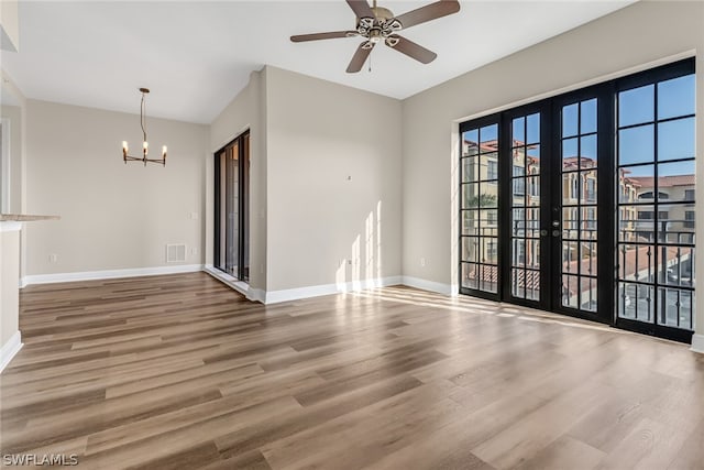 unfurnished room with hardwood / wood-style floors, a healthy amount of sunlight, and ceiling fan with notable chandelier