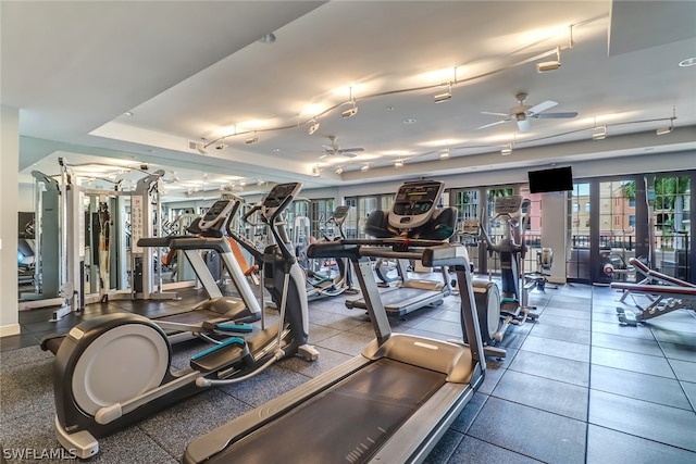 exercise room with tile flooring, ceiling fan, and a tray ceiling