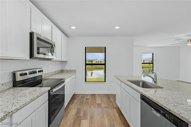 kitchen featuring white cabinets, appliances with stainless steel finishes, light stone counters, light hardwood / wood-style floors, and sink