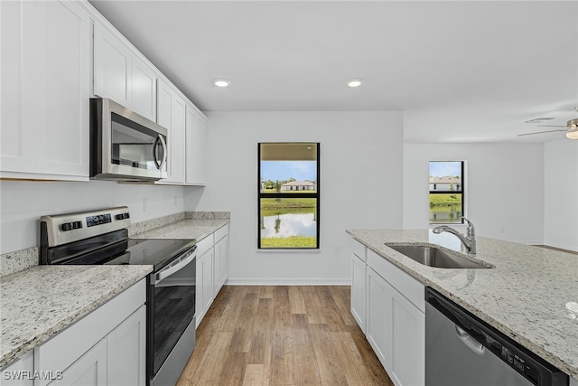 kitchen with a sink, light stone counters, stainless steel appliances, white cabinets, and light wood finished floors