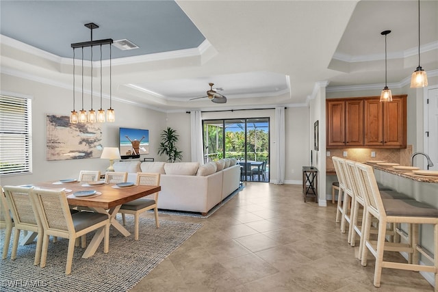 tiled dining room with sink, ceiling fan, ornamental molding, and a tray ceiling