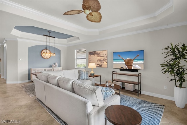 tiled living room with ornamental molding, ceiling fan with notable chandelier, and a raised ceiling