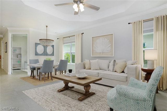 tiled living room with ceiling fan, ornamental molding, and a raised ceiling