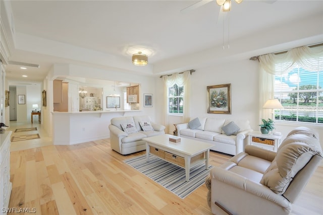 living room with ceiling fan with notable chandelier, a wealth of natural light, and light wood-type flooring