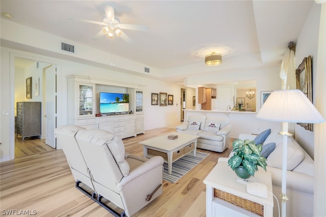 living room featuring a raised ceiling, ceiling fan, and light wood-type flooring