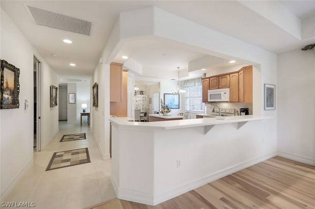 kitchen with a breakfast bar area, light hardwood / wood-style flooring, stove, kitchen peninsula, and a chandelier