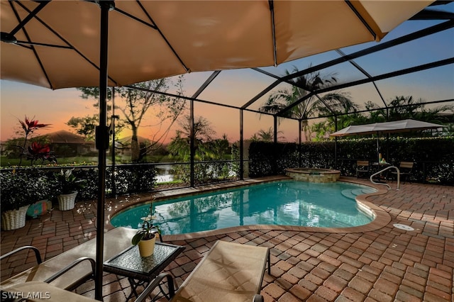 pool at dusk with glass enclosure, a patio area, and an in ground hot tub